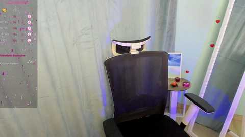 Media: Video of a modern, black ergonomic office chair with a white headrest in a small, cozy room with light blue walls and a desk adorned with red and yellow ornaments.