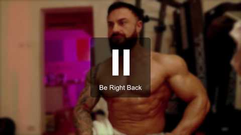 Media: Video of a muscular, bearded man in a gym, shirtless, with visible tattoos. Background features workout equipment and blurred gym setting. Overlay text: \"Be Right Back.\