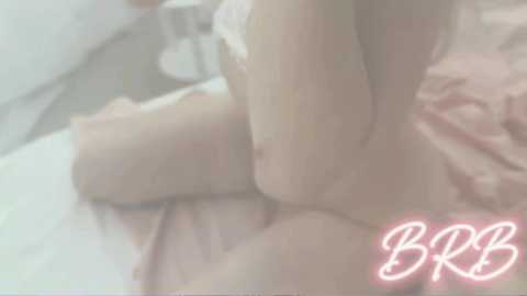 Media: A blurry video of a nude woman lying on a bed, her pale skin and delicate curves partially visible. The background includes a pink sheet and a white pillow, with the initials \"BB\" in pink script at the bottom right.