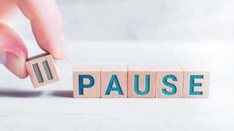 Media: Video of a hand holding a wooden letter \"P\" in front of a stack of wooden letters spelling \"PAUSE.\" The background is a blurred, light-colored wooden floor. The image conveys a sense of stopping or pausing.