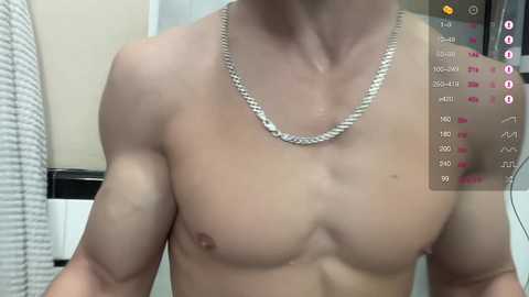 Media: Video of a shirtless, muscular man with light skin and a silver chain necklace, standing in a bathroom with a white towel hanging.