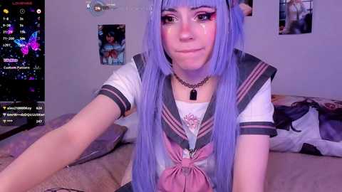 Media: A video of a young woman with long, pastel purple hair, wearing a sailor school uniform, in a bedroom with a TV screen showing a video chat.