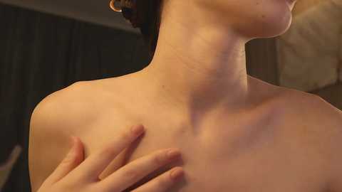 Media: Video of a light-skinned woman with dark hair, partially covered by a black cloth, topless, with her hands gently touching her neck and chest.