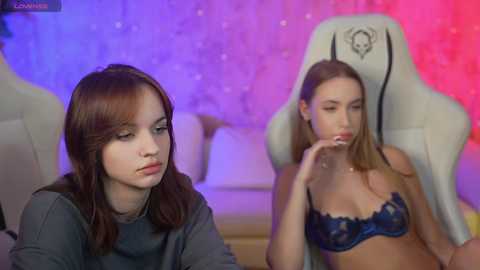 Media: A video shows two young women in a gaming setup: one in a dark top, the other in a blue lace bra, seated in a white gaming chair.