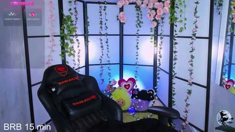 Media: Video of a VR setup featuring a black gaming chair, heart-shaped decorations, and hanging flowers in a room with a grid-like window and soft lighting.