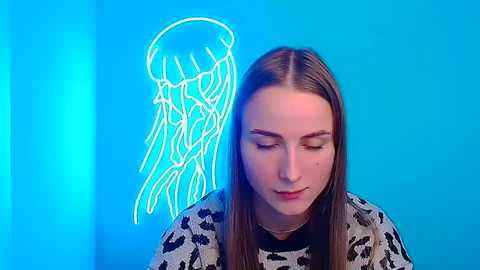 Media: Video of a young woman with straight brown hair, wearing a leopard print shirt, standing against a vibrant blue background with a glowing neon jellyfish outline.