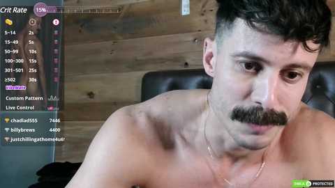 Media: Video of a shirtless man with short, dark hair and a prominent mustache, indoors against a wooden wall, wearing a necklace.