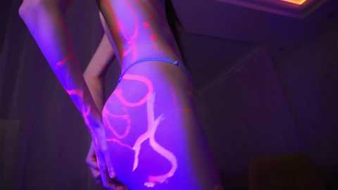 Media: Video of a person's lower back and buttocks with neon pink and purple tribal tattoos under a dimly lit room. The subject is seen from a side angle, highlighting the intricate designs.