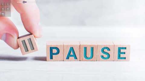 Media: A video shows a hand placing a wooden letter \"U\" on a stack of wooden letters spelling \"PAUSE.\" The letters are light wood with blue \"PAUSE\" text, against a blurred white background.