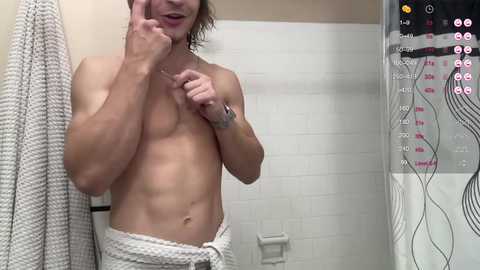 Media: Video of a shirtless, muscular man with wet hair, wearing a white towel, standing in a white-tiled bathroom.