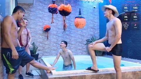 Media: Video of shirtless men in swim trunks playing in a hot tub, with a cowboy hat-wearing man on a stool, surrounded by decorative orange and black pumpkins.