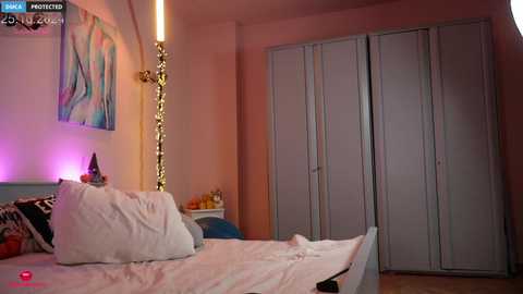 Media: A video of a cozy bedroom with a white bed, colorful pillows, and a large wardrobe. The walls are painted pink, and there's a modern, abstract painting on the left.