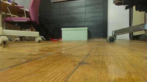 Media: Video of a flooded office floor with wooden planks, featuring a pink office chair and black cabinets, with a white wheeled chair on the right.