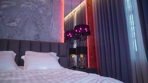 Media: Video of a modern bedroom with a white bed, gray tufted headboard, and gray and purple drapes. A black lamp with multiple hanging globes sits on the nightstand. The wall features a textured mural and soft, ambient lighting.