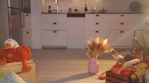 Media: Video of a cozy, rustic kitchen with white cabinets, wooden countertops, and warm lighting. A stuffed animal, potted plant, and a basket of fruits are on the light-colored floor.