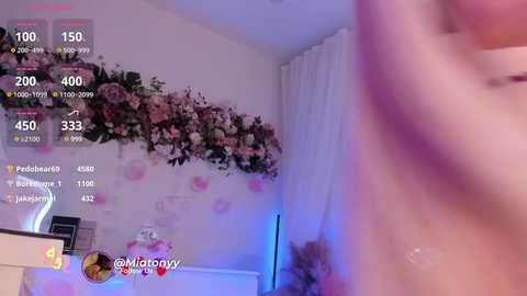 Media: A video of a dimly lit room with a floral arrangement on the left wall, white curtains, and a blurry figure in the foreground.