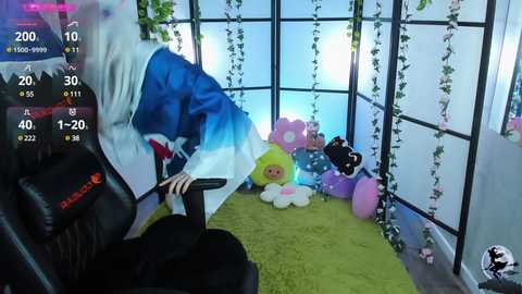 Media: A video of a person wearing a blue and white cosplay costume, sitting on a black chair in a room with a green rug and hanging plants, surrounded by plush toys.