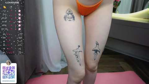 Media: Video of a person in orange thong underwear, showcasing tattoos of a triangle and umbrella on their thighs. Background includes a bed, curtains, and a QR code watermark.