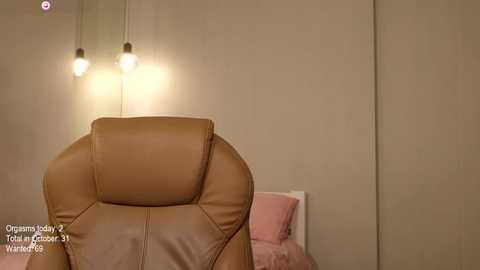 Media: A video of a beige leather recliner chair in a minimalist bedroom with a soft pink bedspread, white wall, and modern pendant lights casting a warm glow.