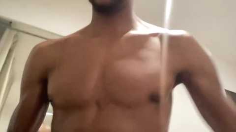 Media: Video of a shirtless, muscular man with medium skin tone and a short beard, standing indoors with a blurred background.