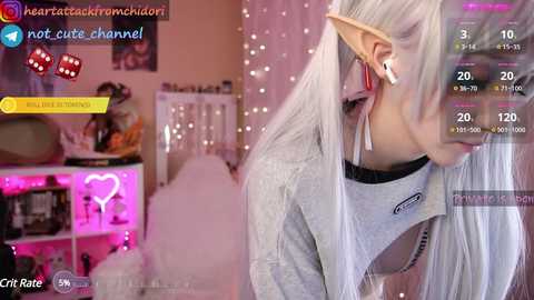 Media: A video of a white woman with long platinum blonde hair, wearing a gray sweatshirt and large elf ears, playing a video game in a cozy room with pink and purple lights.