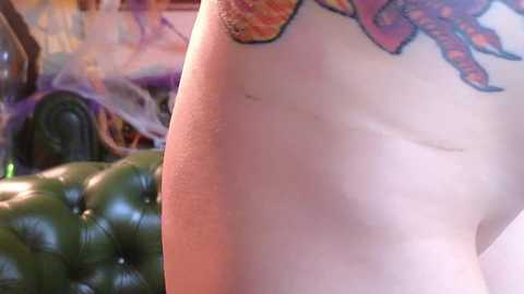 Media: A video of a tattooed person's upper back and arm, showcasing vibrant, colorful tattoos on a light-skinned body. In the background, a green, tufted leather sofa and colorful, abstract art on the wall are visible.