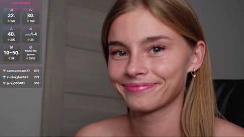 Media: Video of a smiling, fair-skinned woman with straight, blonde hair, wearing a strapless top, indoors against a gray background.