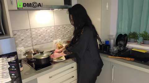 Media: Video of a woman with long black hair in a dark outfit cooking on a modern kitchen stove with tiled backsplash, surrounded by utensils and potted plants.