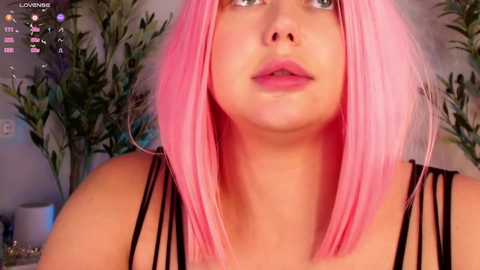 Media: Video of a young woman with fair skin and pink hair, wearing a black strapless top, standing in front of green potted plants, with a \"LOVE\" overlay in the top left.