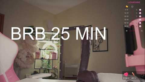 Media: Video of a virtual reality game scene showing a large, dark, phallic object in a beige room with a pink gaming chair, a clock, and a framed picture on the wall. Text reads \"BB25 MIN.\