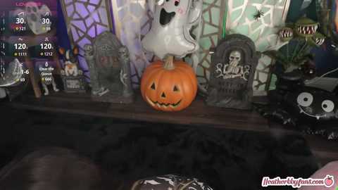 Media: A video depicts a Halloween-themed room with a carved pumpkin, a white ghost, and various spooky decorations on a wooden shelf. The scene includes a health tracker on the bottom right.