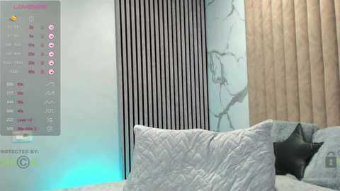 Media: Video of a modern bedroom with a gray bed, beige curtains, and a textured wall with vertical black and white stripes. A digital overlay shows a calendar and weather forecast.