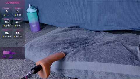 Media: Video of a person using a vibrating sex toy on a grey carpeted floor near a blue couch with a grey towel.