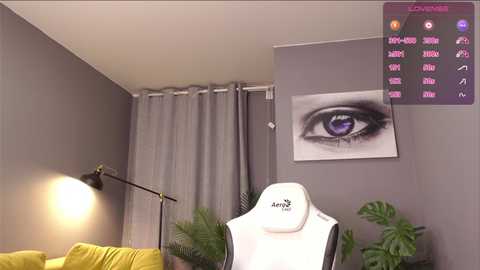 Media: Video of a modern living room featuring a white gaming chair, a large eye art print on a gray wall, a potted plant, and a yellow sofa with a black lamp.