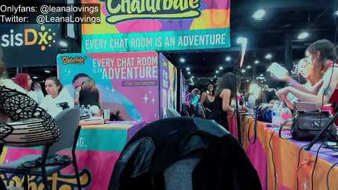 Media: Video of a colorful, crowded convention booth with vibrant decor and multiple attendees, including one person wearing a black jacket and another with a pink jacket.