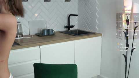 Media: Video of a modern kitchen with white cabinets, wooden countertop, black sink, and green chair; a person's face partially visible on the left.