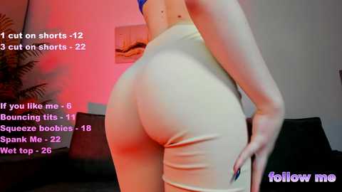 Media: Video of a light-skinned woman with large buttocks in tight beige leggings, standing in a dimly lit room with red lighting. Text overlay suggests she's wearing shorts.