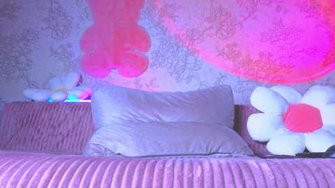 Media: Video of a cozy, pastel-themed bedroom with a bed covered in light purple blankets, adorned with large, fluffy white and pink flowers.