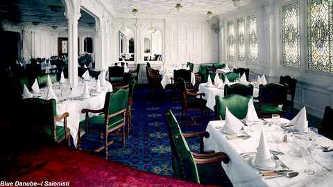 Media: Video of an ornate dining room with white walls, green velvet chairs, blue patterned carpet, white tablecloths, white napkins, and intricate stained-glass windows.