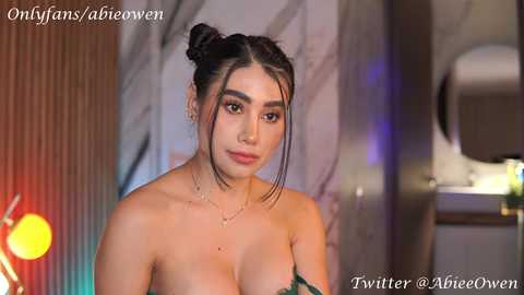 Media: Video of a young woman with dark hair in two buns, wearing a strapless green dress, posing indoors with blurred background. Text overlays: OnlyFans/@abriewen, Twitter/@ArieeOwen.