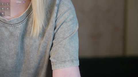 Media: Video of a woman with long, straight blonde hair wearing a grey T-shirt, with a blurred background featuring a beige wall.