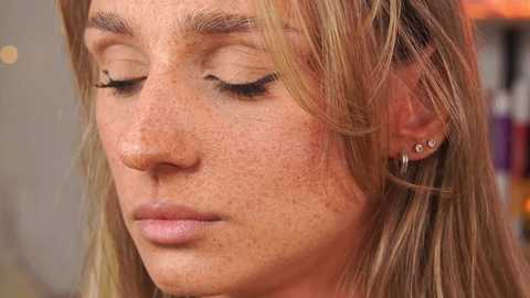 Media: Video of a young woman with fair skin, freckles, and blonde hair, wearing minimal makeup, showing a contemplative expression.