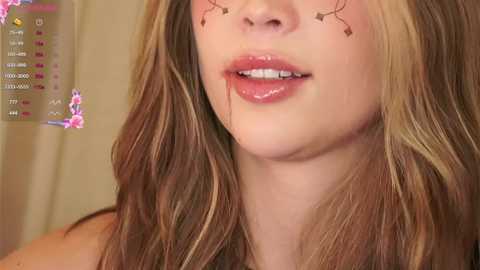 Media: Video of a young woman with long, wavy brown hair, light skin, and glossy pink lips, adorned with star-shaped facial stickers. The background shows a blurred, beige curtain.