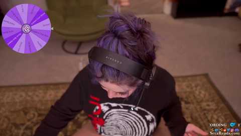 Media: A video of a person with purple hair wearing a black headset, sitting on a patterned rug, performing oral sex on a man in a black shirt with a graphic design.