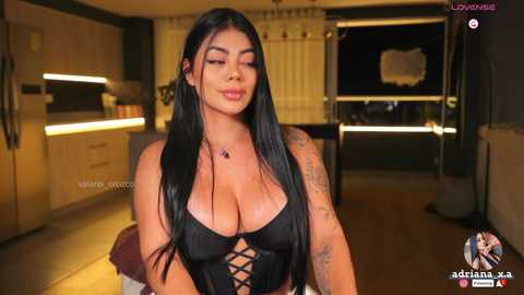 Media: Video of a Latina woman with long black hair, wearing a black lace-up corset revealing ample cleavage, standing in a modern kitchen with sleek wooden cabinets and warm lighting.