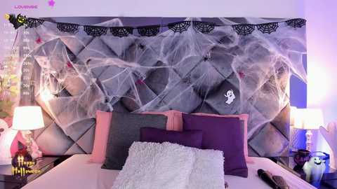 Media: Video of a Halloween-themed bedroom with a plush, gray tufted headboard draped in white spider webs, purple pillows, and a plush white throw.