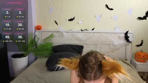 Media: A video of a woman in a cat costume lying on a bed with Halloween decorations, including a carved pumpkin, bats, and fake spiderwebs.