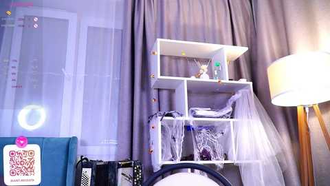 Media: Video of a tidy, modern nursery with white shelves, a white crib, white curtains, a teal chair, and a white lamp.