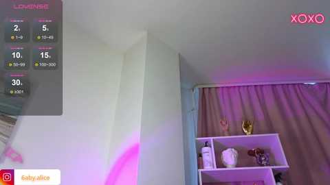 Media: Video of a modern, minimalist bedroom with white walls, purple curtains, and a white shelving unit holding a vase and books. A virtual reality headset display shows a \"LOVEMATE\" game with various temperature options.