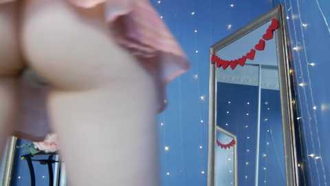 Media: A blurred video of a mirror reflecting a person lifting a pink shirt, with a red heart garland and clock in the background.